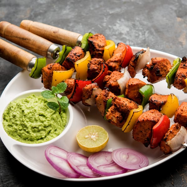 Haandi's chicken tikka skewers with bell peppers and onions, served with green chutney, lime, and red onion.