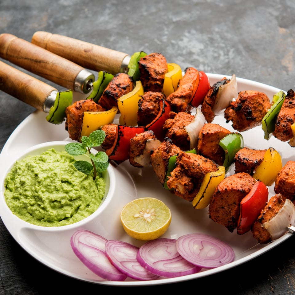 Haandi's chicken tikka skewers with bell peppers and onions, served with green chutney, lime, and red onion.