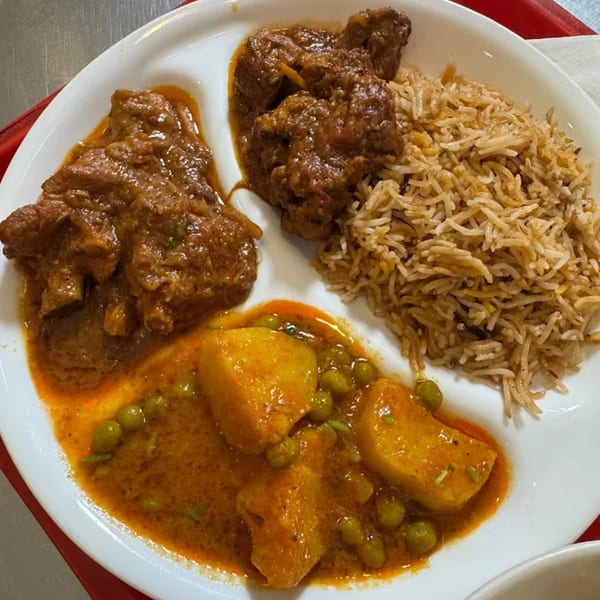 A white plate with three sections of Pakistani food: meat curry, rice, and potato and pea curry.