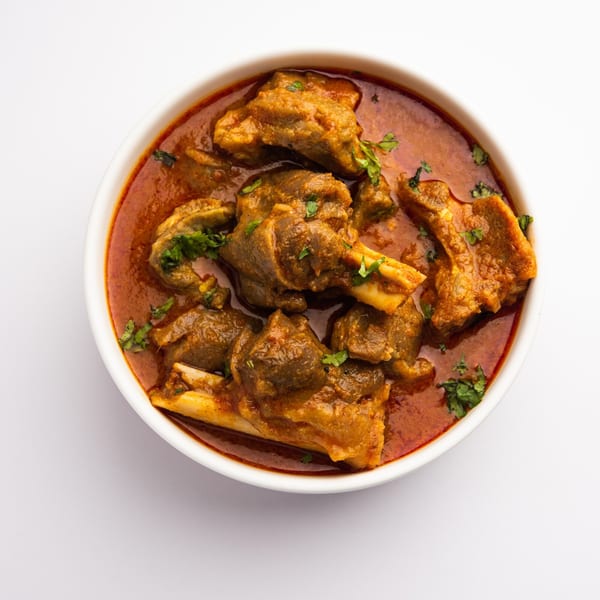 A white bowl filled with Pakistani mutton curry, garnished with fresh cilantro, on a white background.