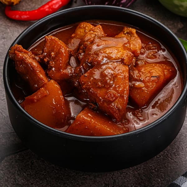 A black bowl filled with Haandi's Pakistani chicken and potato curry in a rich, dark sauce.