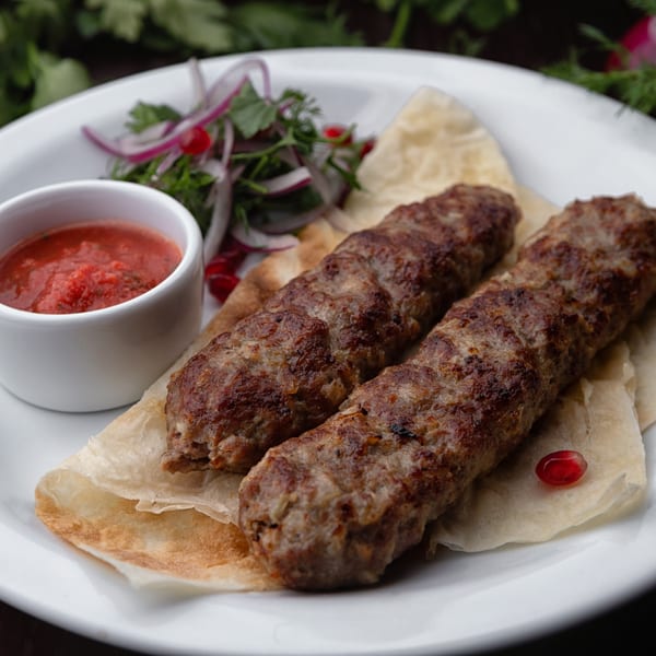 Two Haandi seekh kebabs on flatbread with red sauce and a side salad on a white plate.