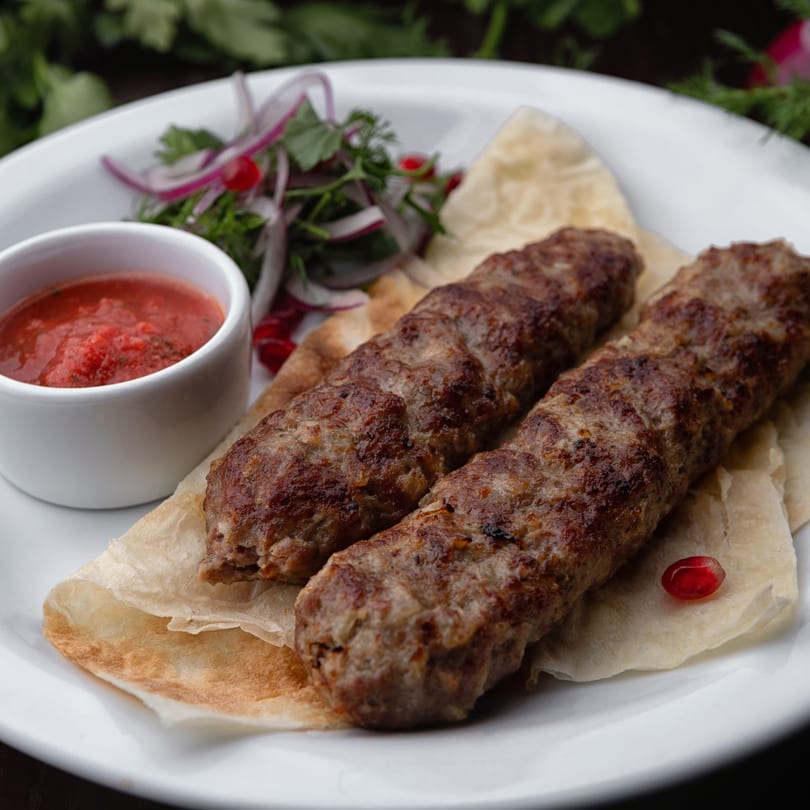 Two Haandi seekh kebabs on flatbread with red sauce and a side salad on a white plate.